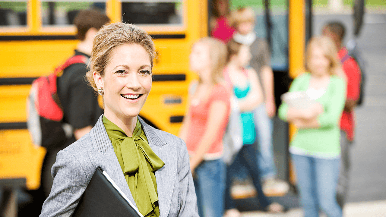 School administrator outside as kids board a school bus.