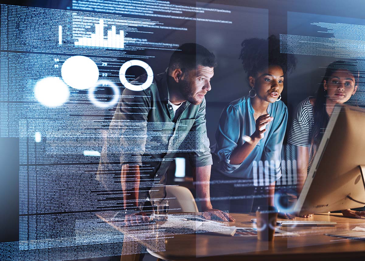 Three people lean on a desk as they collaborate on a high-tech computer in a dimly-lit room.