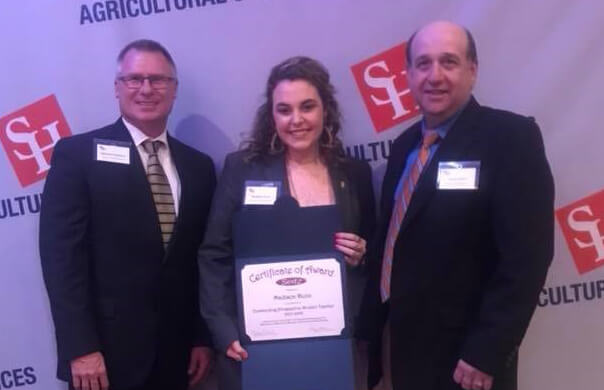 Madison Dunn poses in front of an SHSU award wall holding a fresh certificate of award.