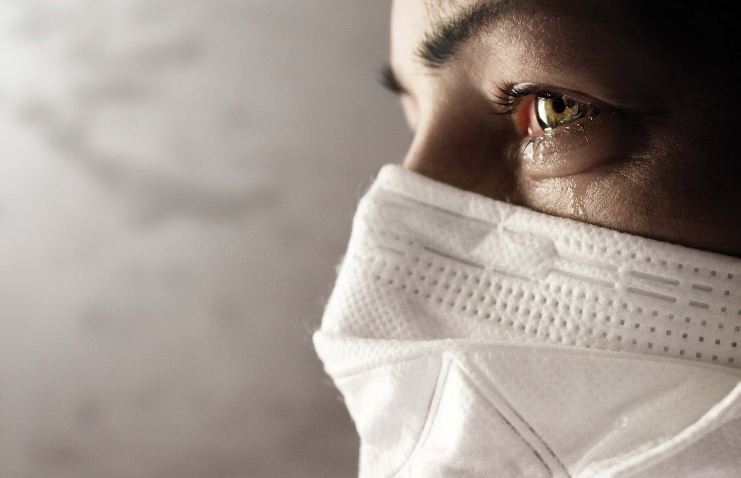 A close-up view of a person wearing a mask. They have a tear coming down their cheek.