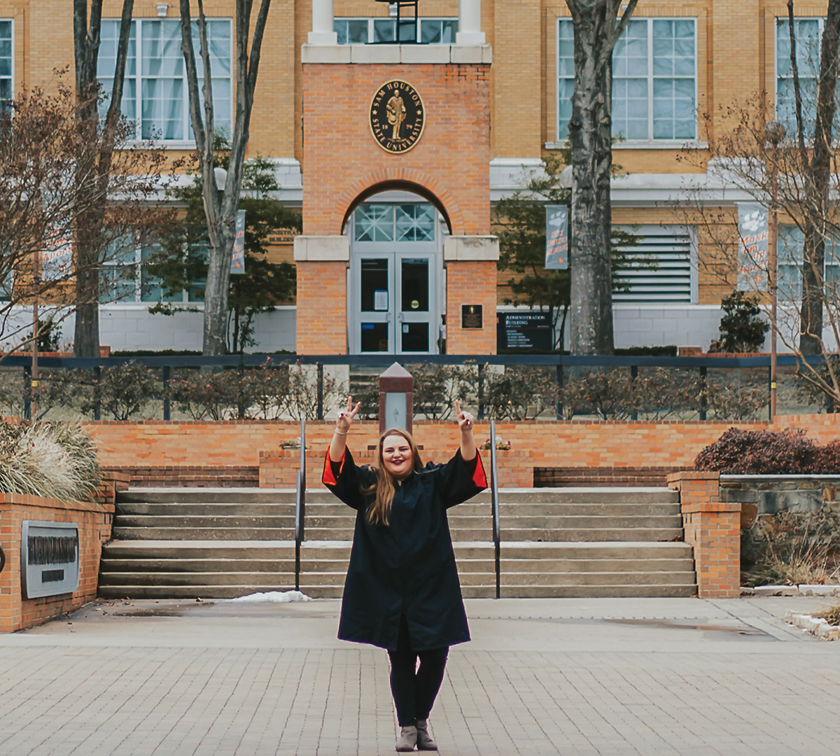 Amber Hoffman wearing graduation attire in front of the SHSU clocktower.