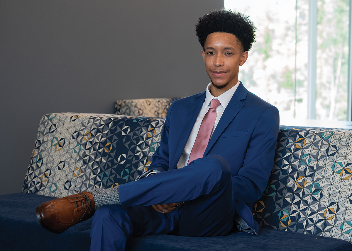 Nehemiah Juniel wears a graduation cap in front of the Administration Building on the Sam Houston State University campus. He smiles proudly.